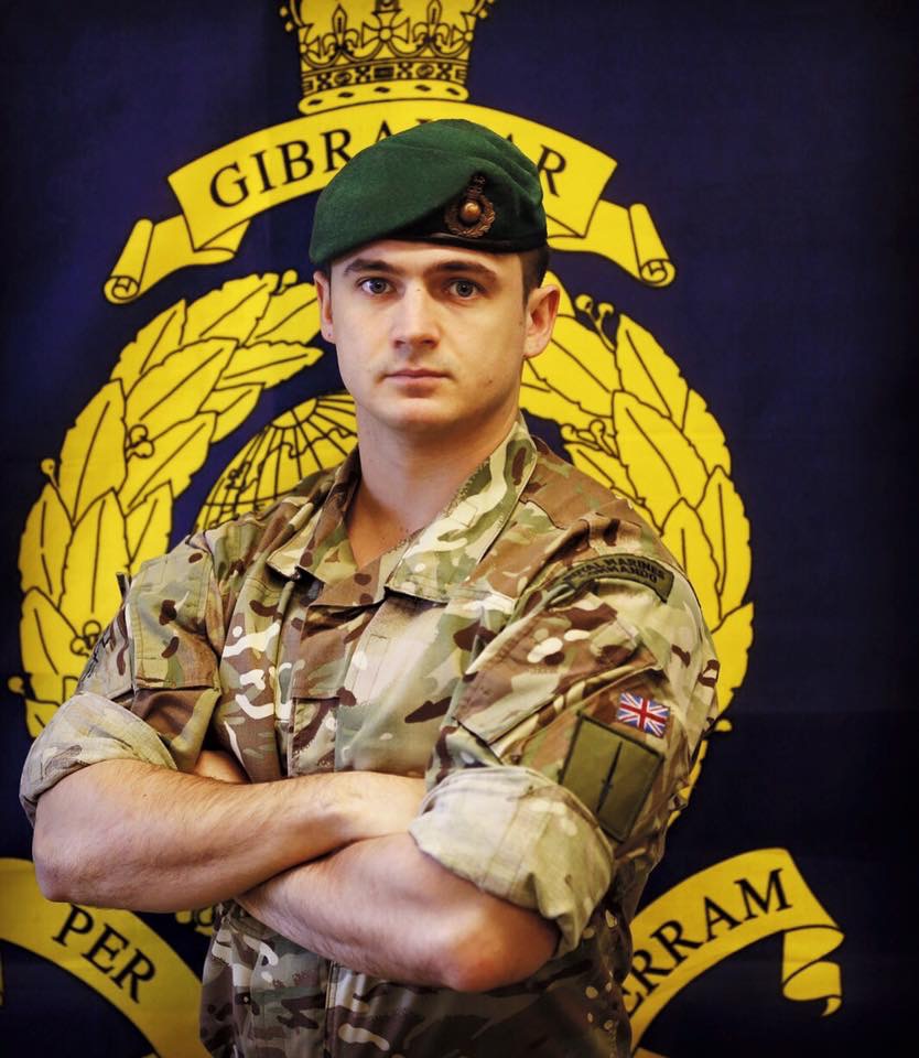 Mark Wheeler in his Royal Marines uniform, stood in front of the Corps crest
